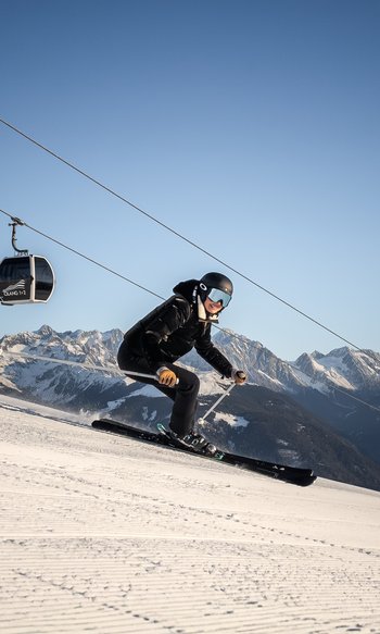 Skier on slope with cable car and snow-covered mountains in the background