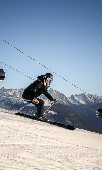 Die Heimat des Strahlens: Ihr Wellnesshotel in Südtirol Skifahrer fährt eine Piste mit Seilbahn und verschneiten Bergen im Hintergrund