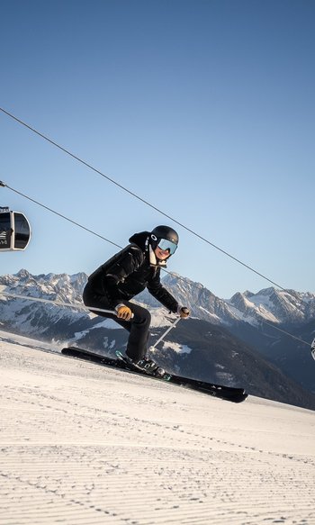 Skier on slope with cable car and snow-covered mountains in the background