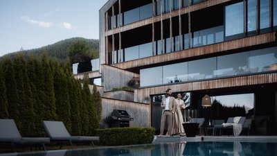 L’esclusività in foto: il nostro chalet in Alto Adige di lusso Coppia in piedi vicino alla piscina davanti a casa moderna in legno