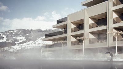 Photos from your hotel in Pfalzen in Val Pusteria/Pustertal Modern hotel building with mist over pool and snowy mountains in the background