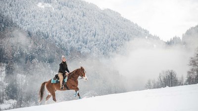 Donna a cavallo sulla neve davanti a foresta e montagne innevate
