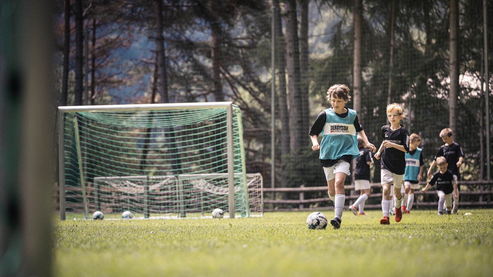 Kinder spielen Fußball auf einem Rasenplatz mit mehreren Toren und Bällen