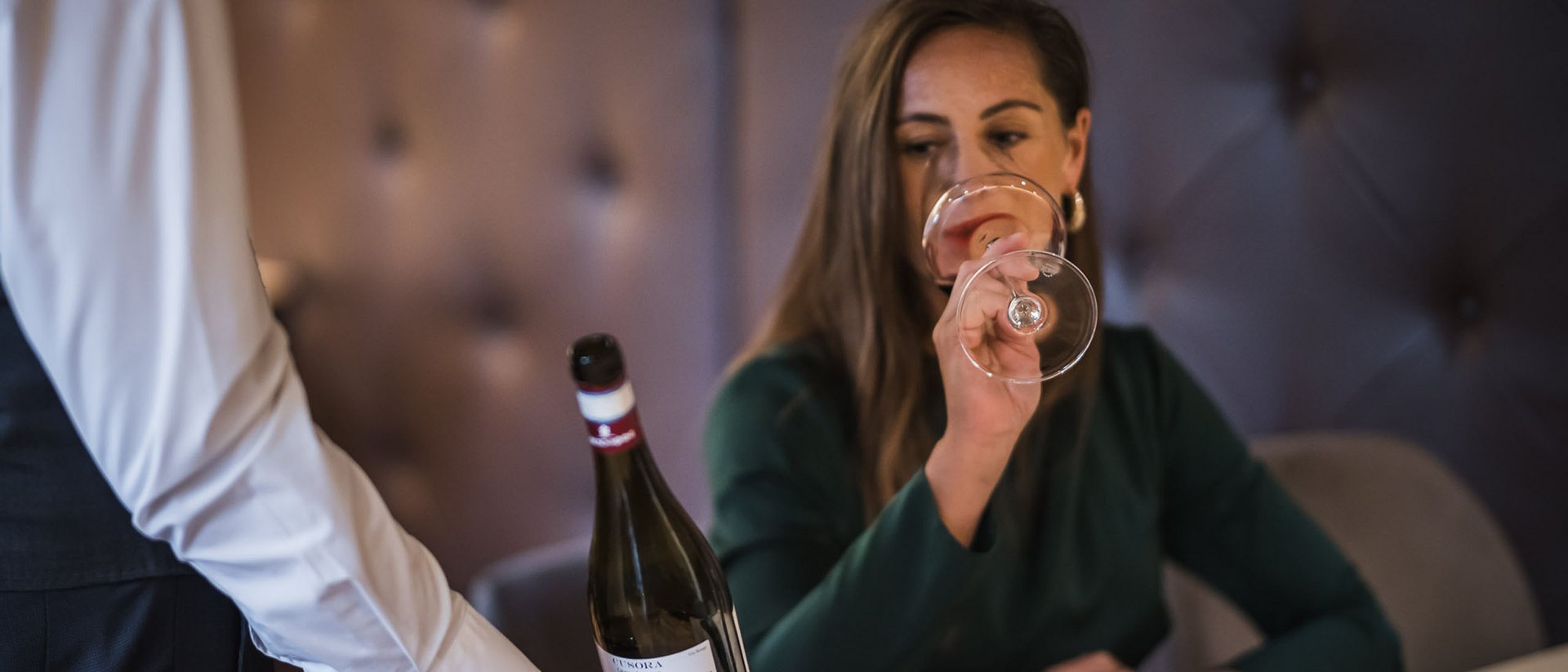Frau probiert Rotwein, während Kellner eine Flasche hält