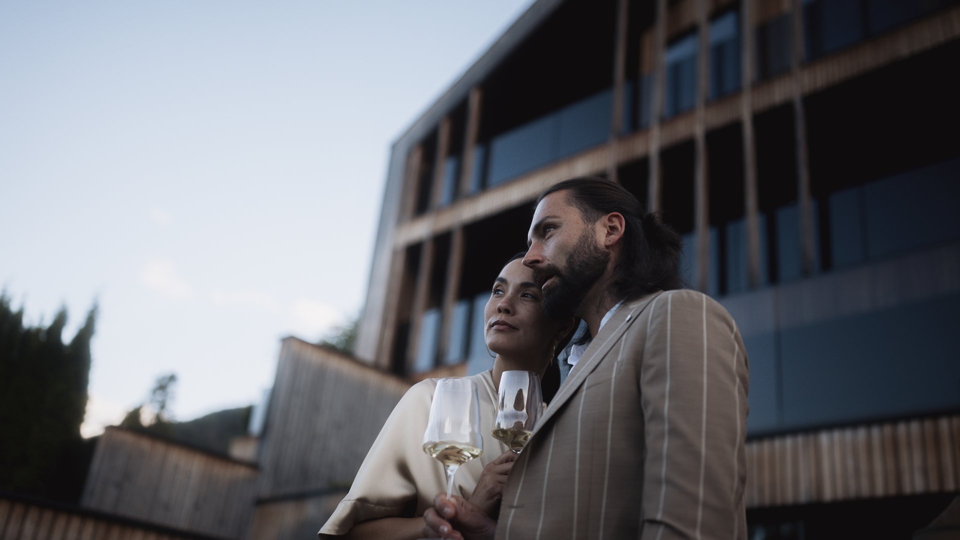 Paar mit Wein vor modernem Gebäude bei Sonnenuntergang