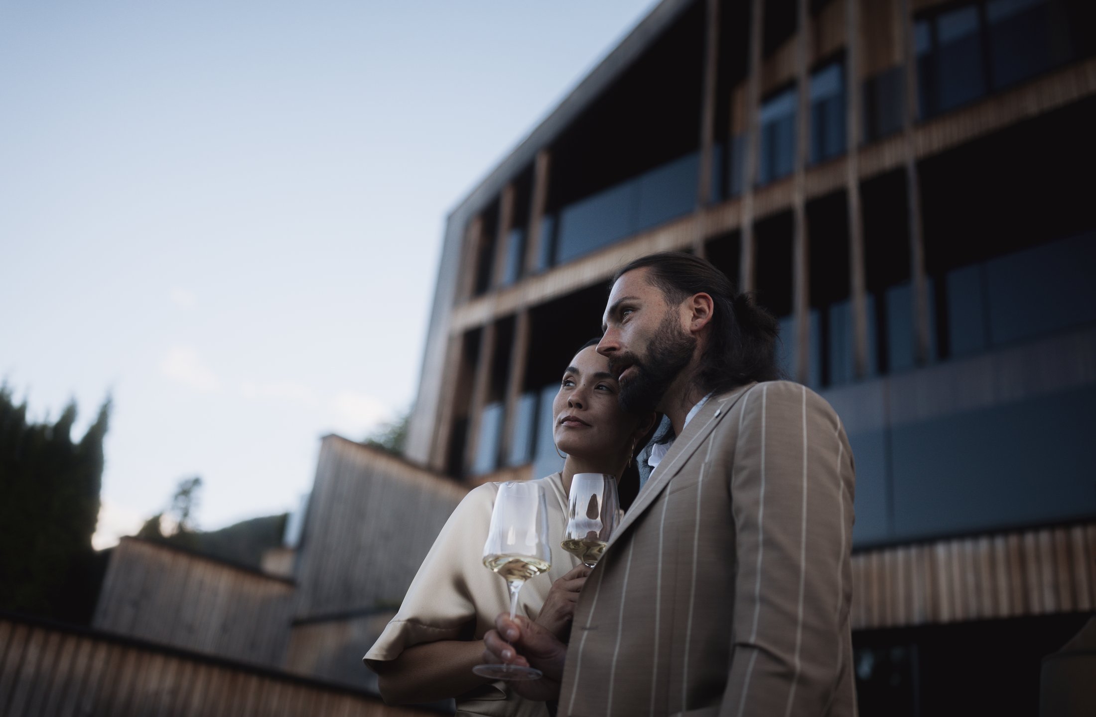 Coppia con vino davanti a edificio moderno al tramonto