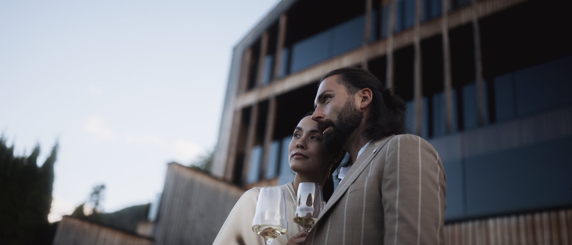 Paar mit Wein vor modernem Gebäude bei Sonnenuntergang