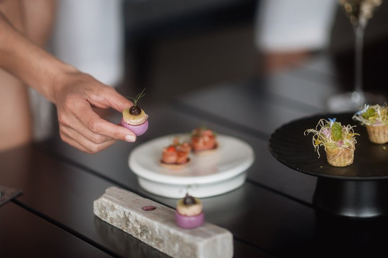 Hand hält ein kleines, farbenfrohes Gourmet-Häppchen an einem gedeckten Tisch