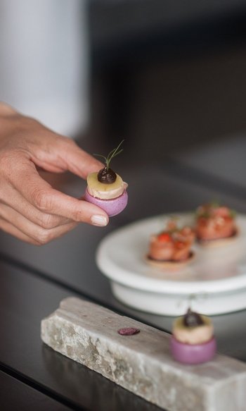 Hand holding a small colorful gourmet bite on a set dining table