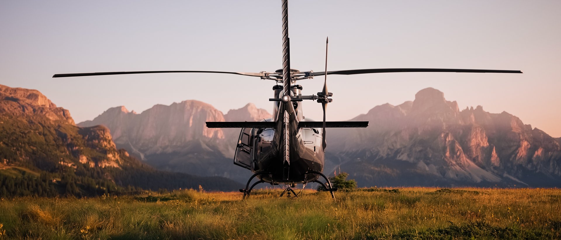 Vista posteriore di un elicottero su un prato con montagne al tramonto