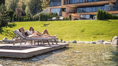 L’esclusività in foto: il nostro chalet in Alto Adige di lusso Coppia si rilassa su lettini vicino a uno stagno davanti a casa moderna in montagna