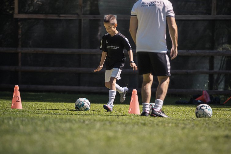 Child practicing soccer with coach on green grass field
