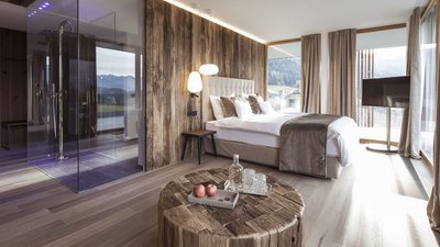 Camera d'hotel moderna con parete in legno, letto grande e doccia con vista sulle montagne