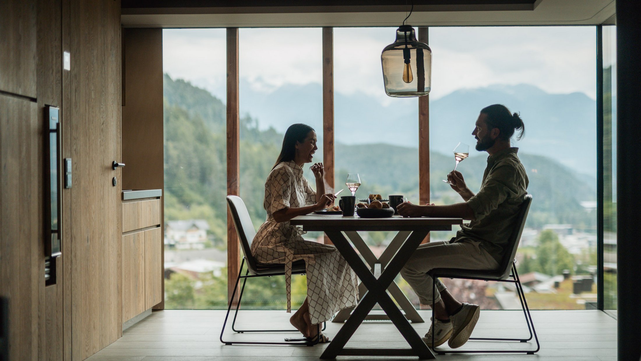 Coppia che beve vino e mangia insieme con vista sulle montagne in sala da pranzo moderna