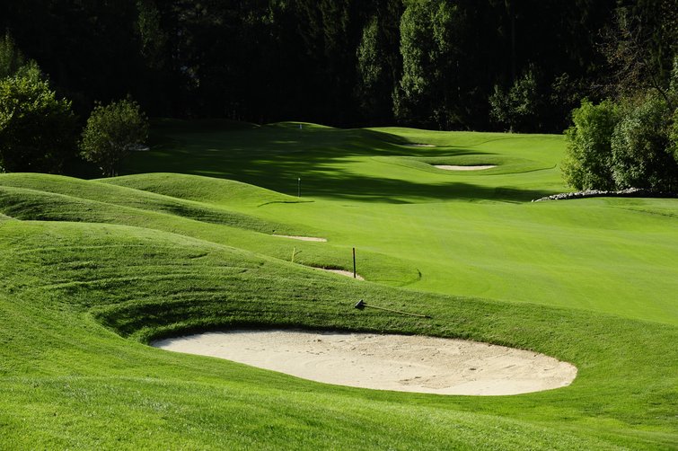 Servizi premium per il golf nel nostro hotel in Alto Adige Campo da golf con bunker di sabbia e prato curato davanti agli alberi