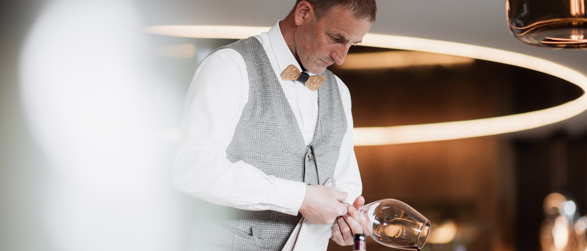 Man in vest and bow tie pouring wine into a glass in an elegant restaurant