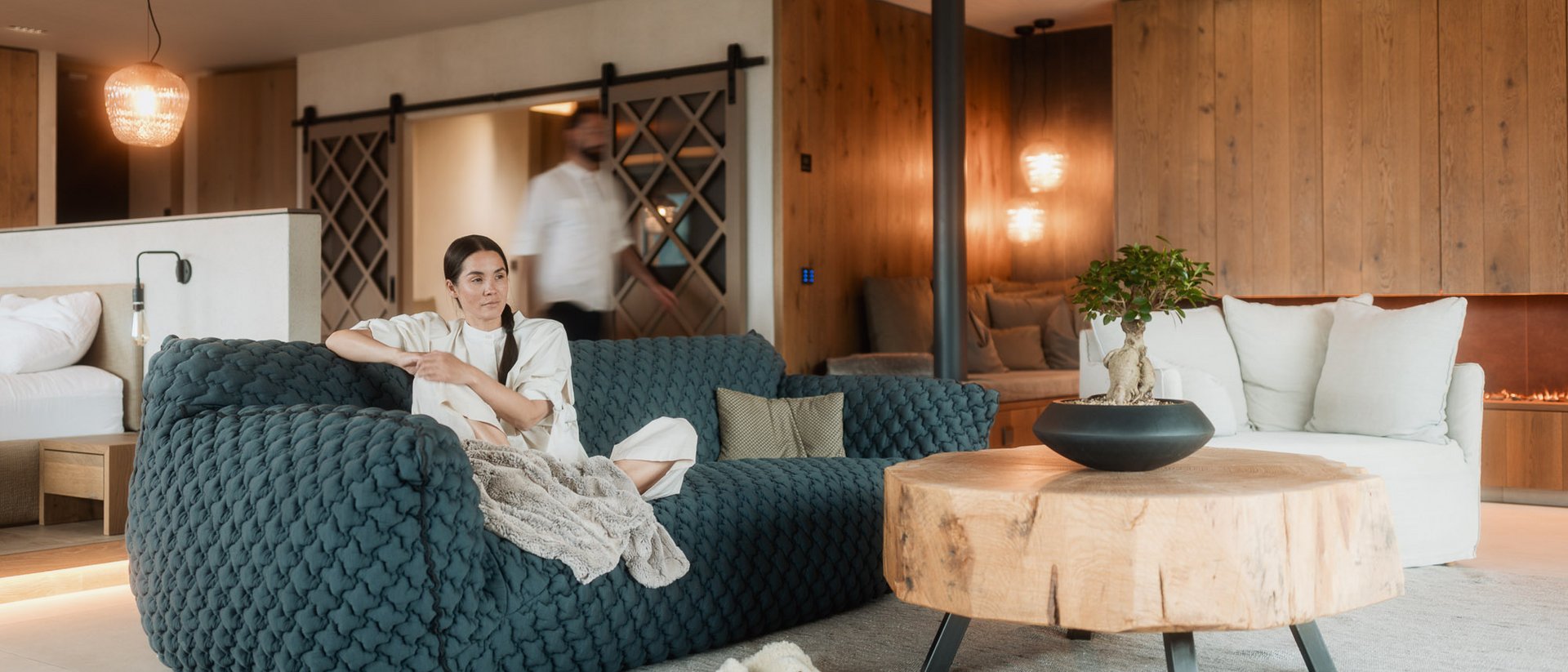 Eine regenerierende Auszeit vor Weihnachten Frau sitzt auf blauem Sofa in modernem Wohnzimmer mit Holztisch und Kamin