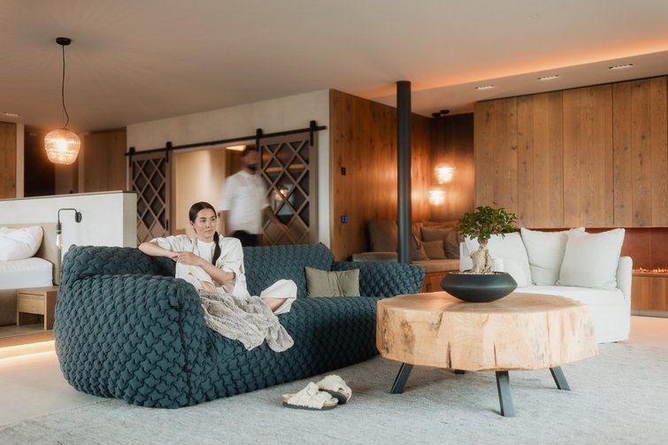 Frau sitzt auf blauem Sofa in modernem Wohnzimmer mit Holztisch und Kamin