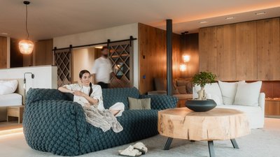 L’esclusività in foto: il nostro chalet in Alto Adige di lusso Donna seduta su divano blu in soggiorno moderno con tavolo di legno e camino