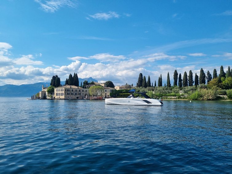 Barca sul lago con isola e montagne sullo sfondo sotto cielo sereno