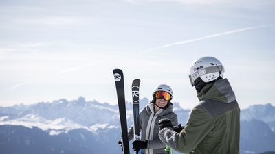 Due sciatori con abbigliamento invernale davanti a montagne innevate sotto un cielo limpido