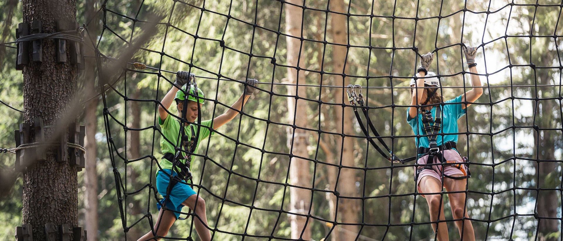 Due bambini arrampicano su una rete di corde in un parco avventura nel bosco