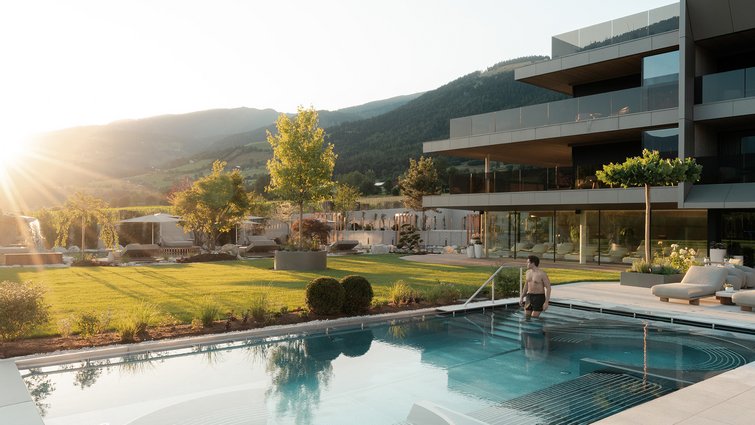 Man entering pool next to modern house at sunset in mountain landscape