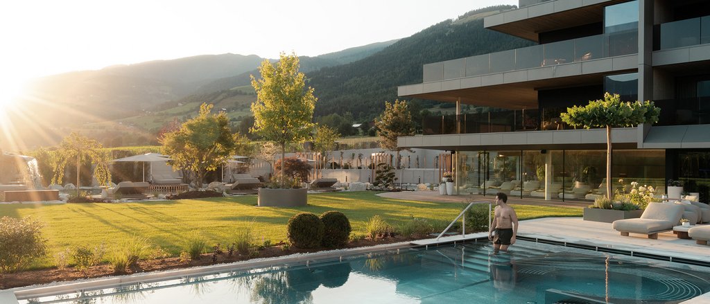 Der facettenreiche Spa unseres Spa-Hotels in Südtirol Mann geht in Pool neben modernem Haus bei Sonnenuntergang in Berglandschaft