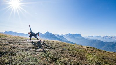 Donna che fa yoga su un tappetino in montagna con sole intenso