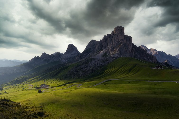 Green meadows with rocky mountains and dark cloudy sky