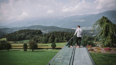Uomo piedi nudi su terrazza con ringhiera in vetro e vista su colline verdi
