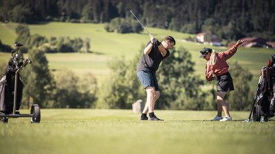 Uomo che fa un colpo di golf con mazza, donna che dimostra lo swing su campo verde