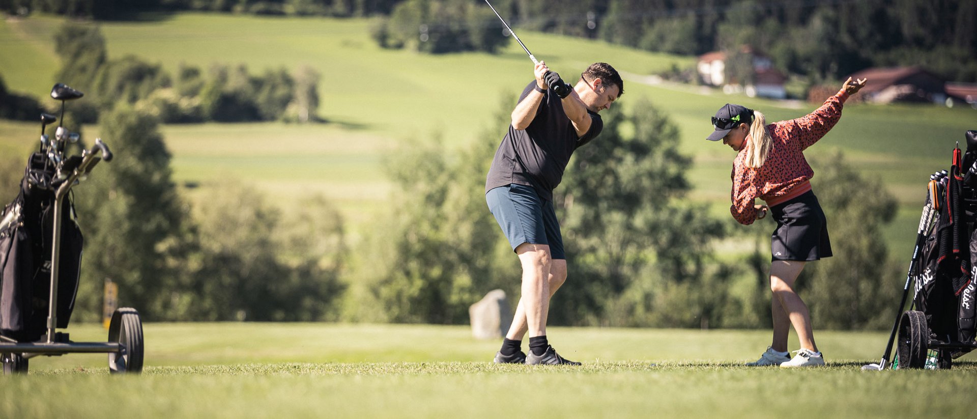 Your source of enrichment: our hotel at Mt Plan de Corones Man swinging golf club, woman demonstrating golf swing on green golf course