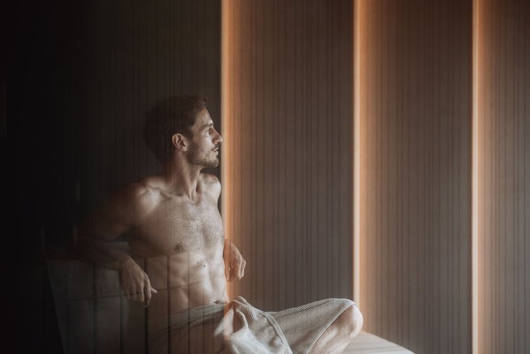 Uomo rilassato seduto in sauna con asciugamano in vita