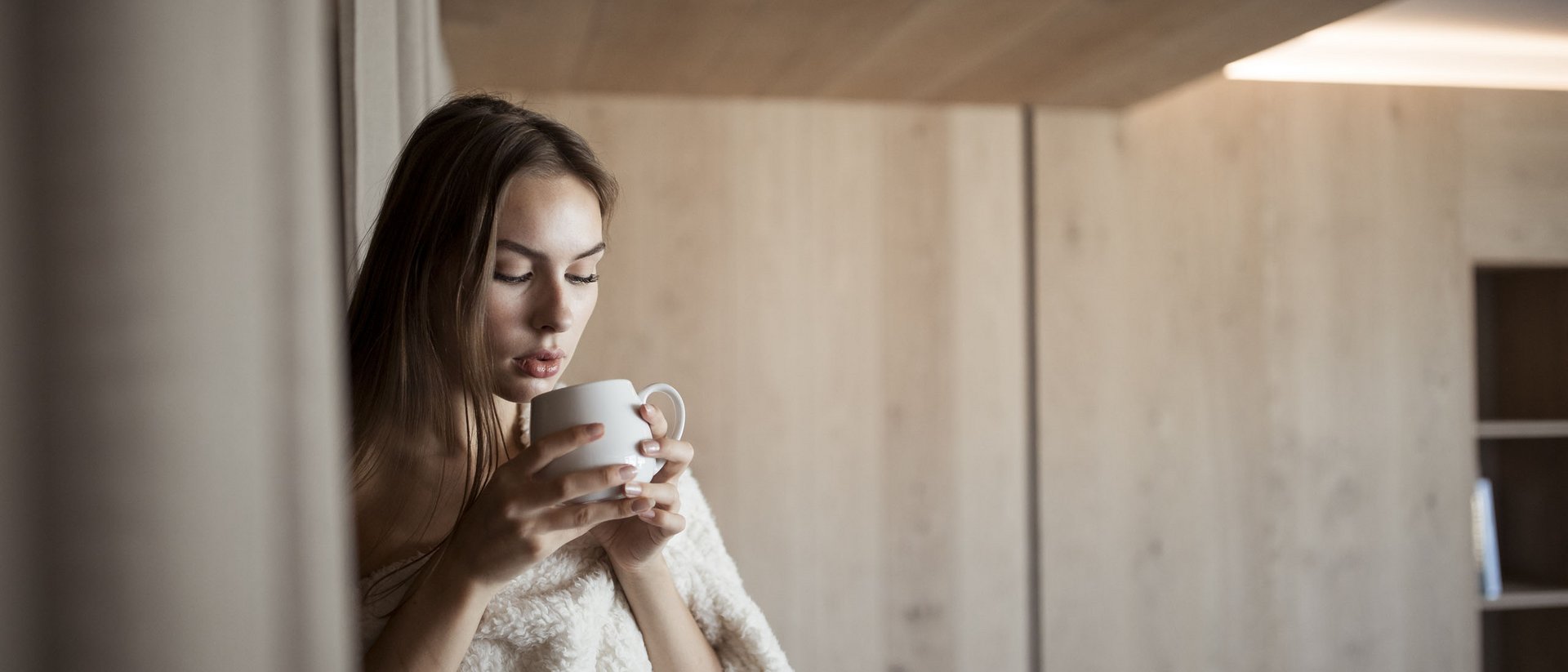 Donna con coperta che beve da una tazza in ambiente accogliente