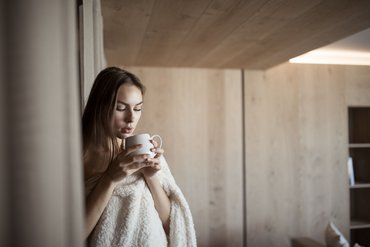Frau in Decke trinkt aus Tasse in gemütlichem Raum