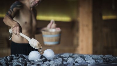 Uomo versa acqua sulle pietre calde nella sauna