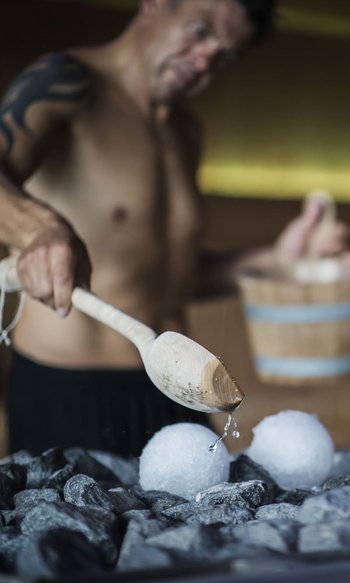 Man pouring water on hot stones in sauna