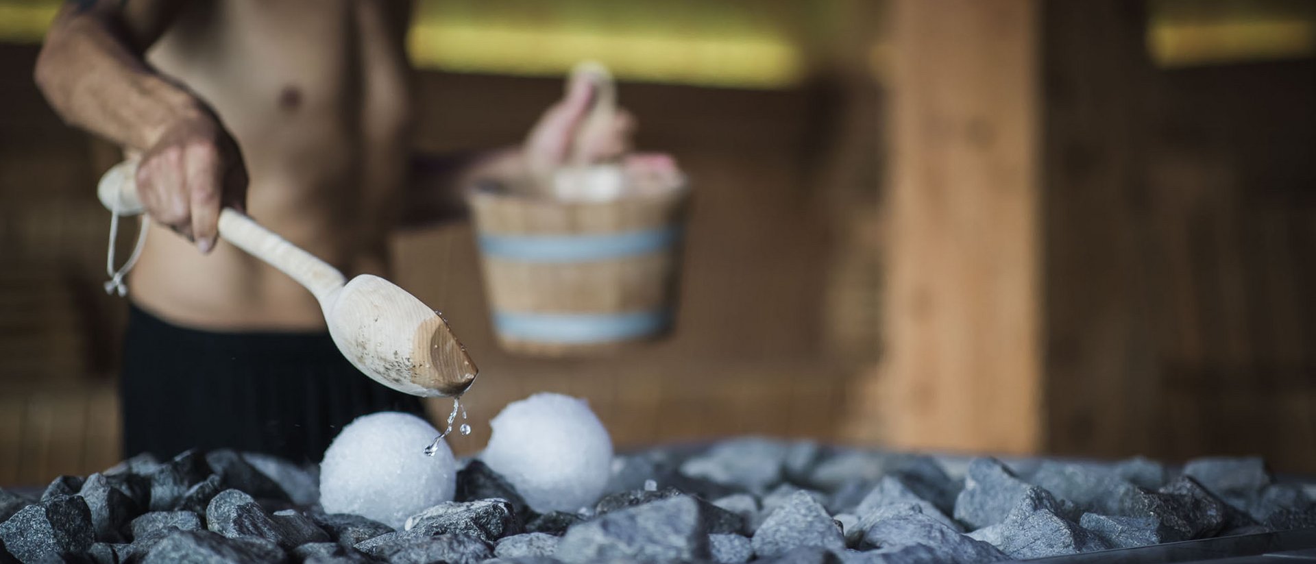 Man pouring water on hot stones in sauna