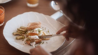 Person cutting breakfast with poached egg, toast, and vegetables on plate