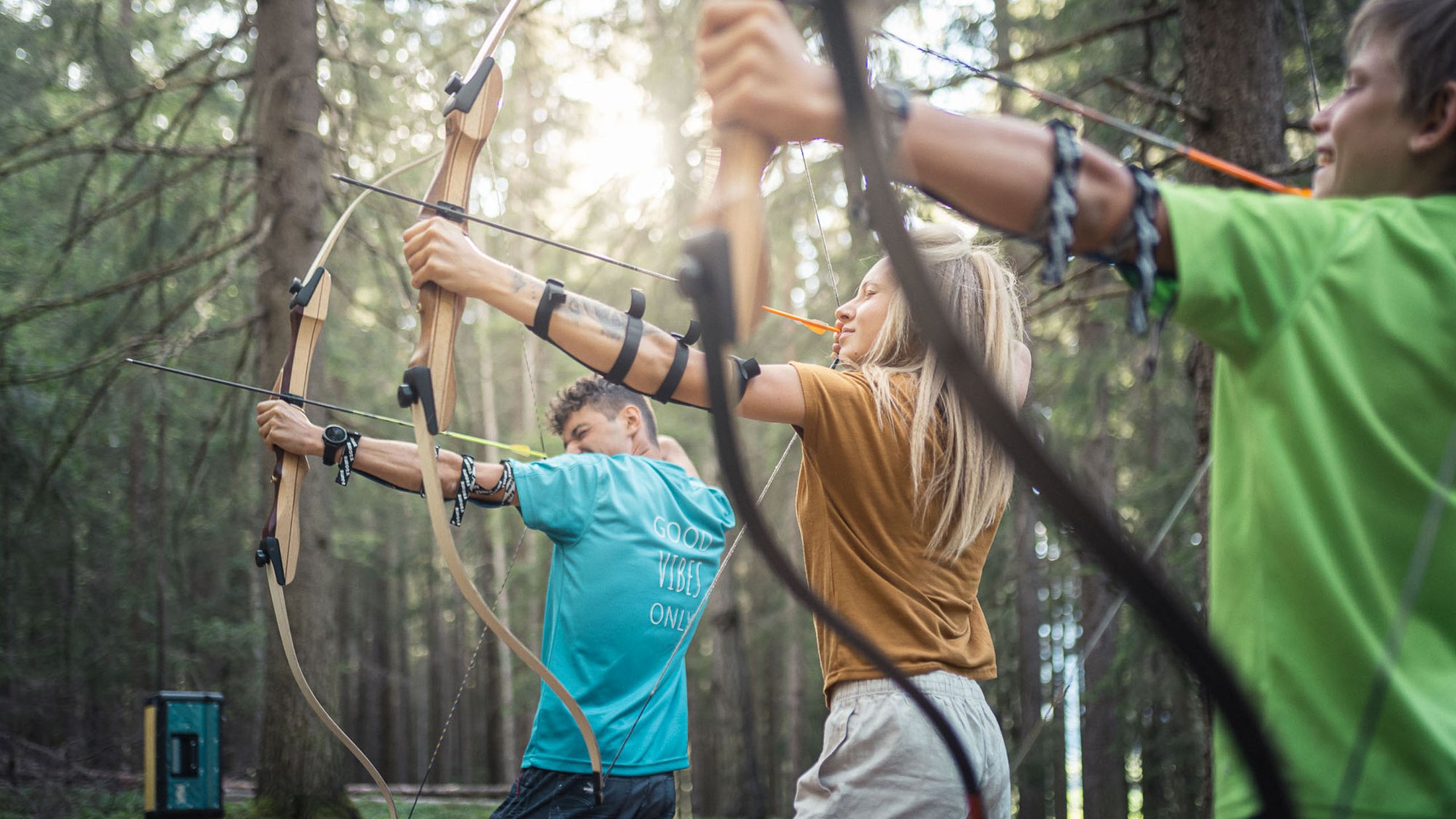 Drei Personen beim Bogenschießen im Wald