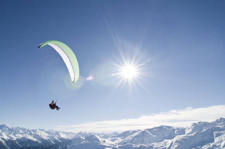 Persona in parapendio sopra montagne innevate con cielo soleggiato