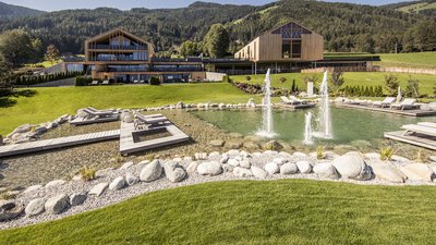 Hotel moderno con piscina naturale e fontane davanti a panorama montano boscoso