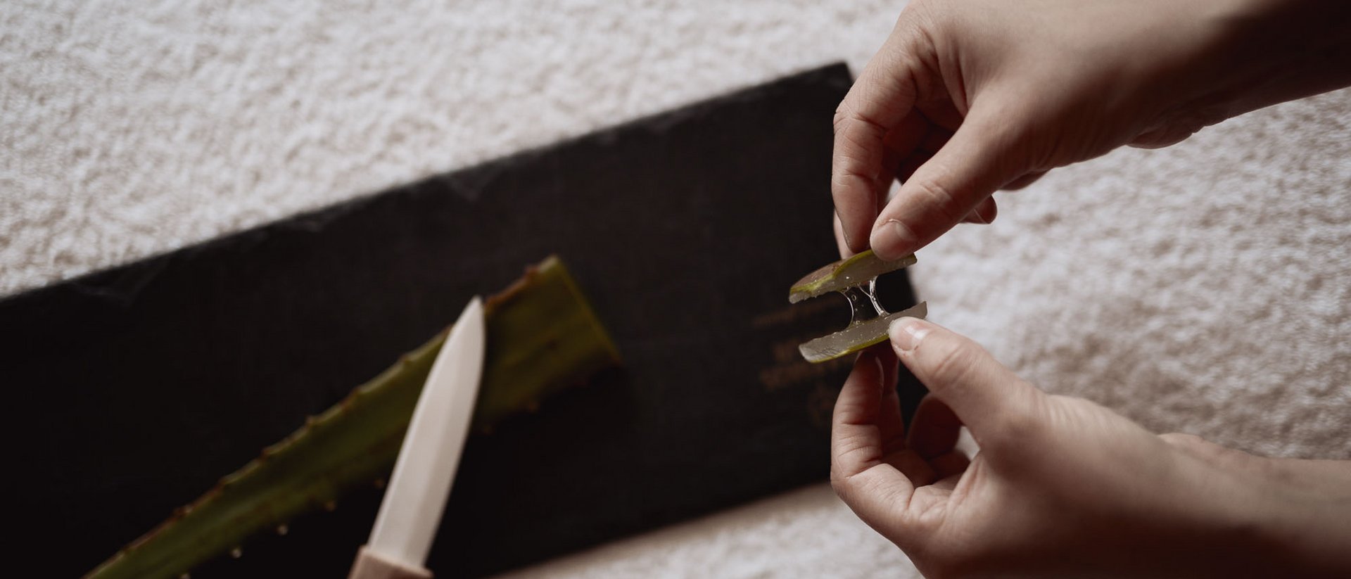 Hände halten in zwei Hälften geschnittenes Aloe-Vera-Blatt mit Gel