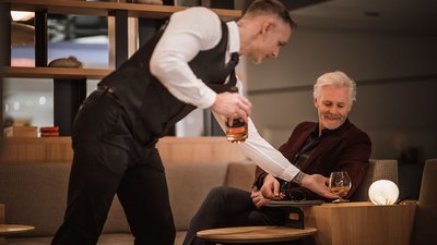 Cameriere serve una bevanda a un uomo anziano in una lounge