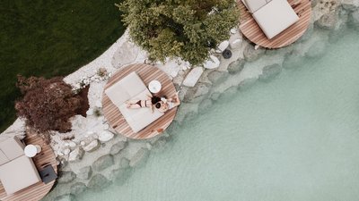 Two people relaxing on lounge chairs by clear water in a garden