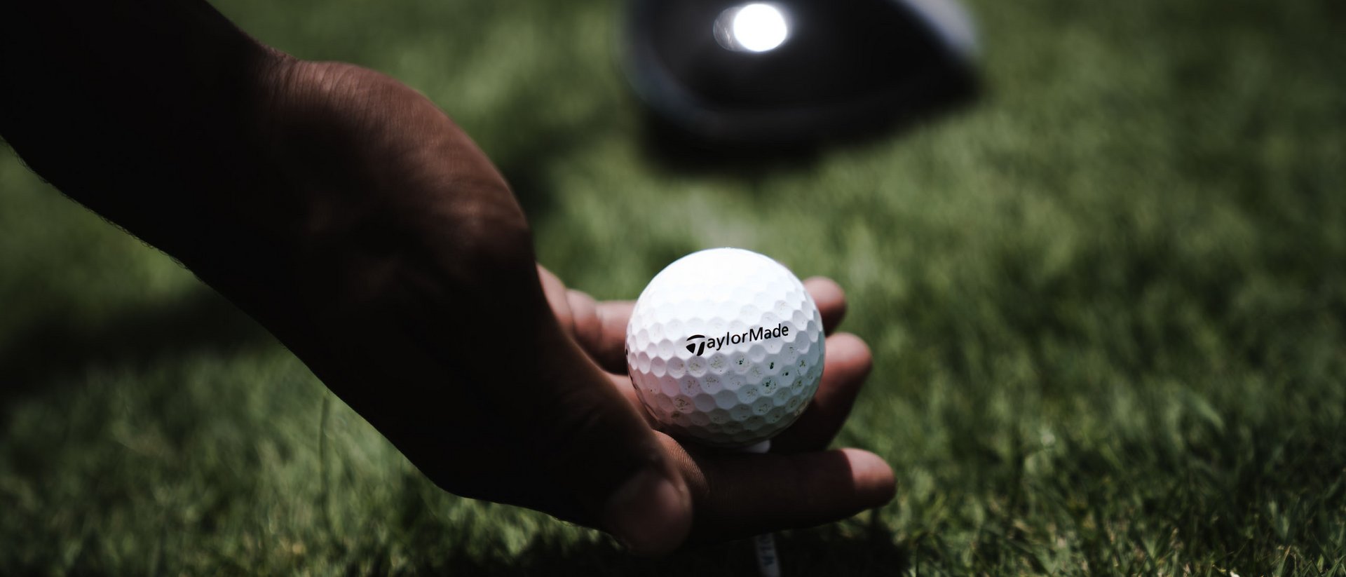 Hand legt Golfball auf Abschlag auf grünem Gras mit Golfschläger im Hintergrund