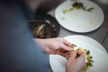 Hands plating edible flowers and vegetables on dish in professional kitchen