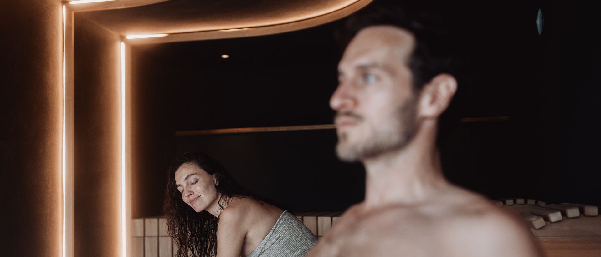 Die Heimat des Strahlens: Ihr Wellnesshotel in Südtirol Frau und Mann entspannen in einer modernen Sauna mit warmem Licht