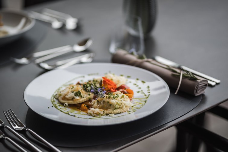 Fein angerichtete Ravioli mit Kräutern und essbaren Blüten auf weißem Teller